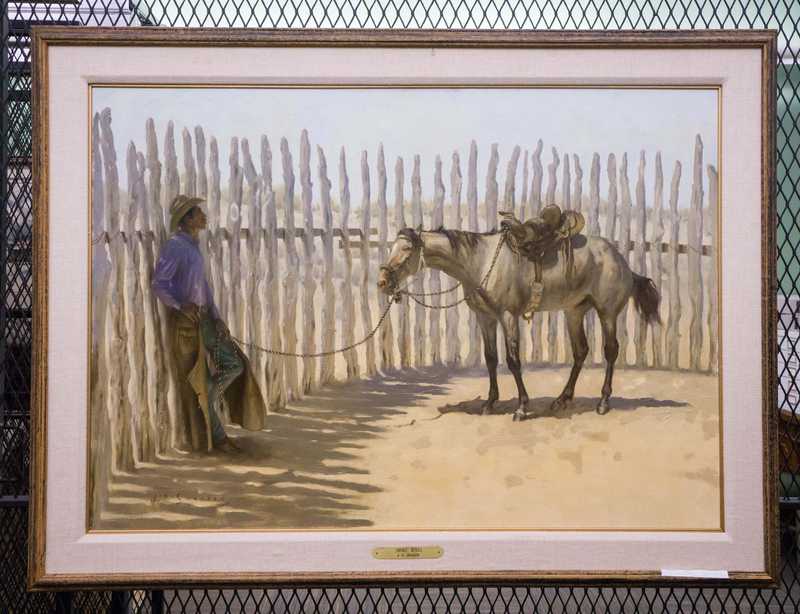 Depicts cowboy leaning on fence